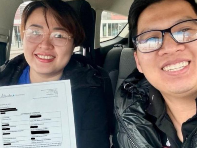 Gia đình chị Hùng cầm giấy đề cử tỉnh bang Alberta sau 6 tháng làm việc, ngồi trong xe tại Canada, rạng rỡ với nụ cười chiến thắng.